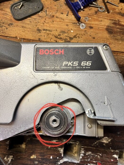 Bosch cirkelsåg på arbetsbänk, saknar sågblad, verktyg och skruvar synliga, röd cirkelmarkerad del av sågen.