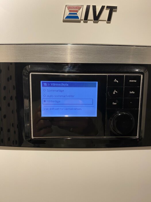 IVT värme/kylsystem panel med menyval för sommarläge, automatiskt eller vinterläge. Reflektion, troligen inomhus.