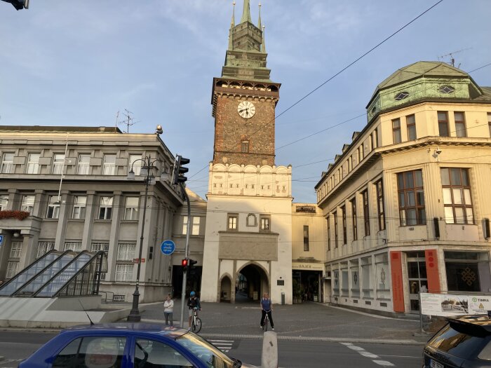 Stadsbild med historisk tornbyggnad, personer, bilar, cyklar, övergångsställe och modern samt gammal arkitektur.