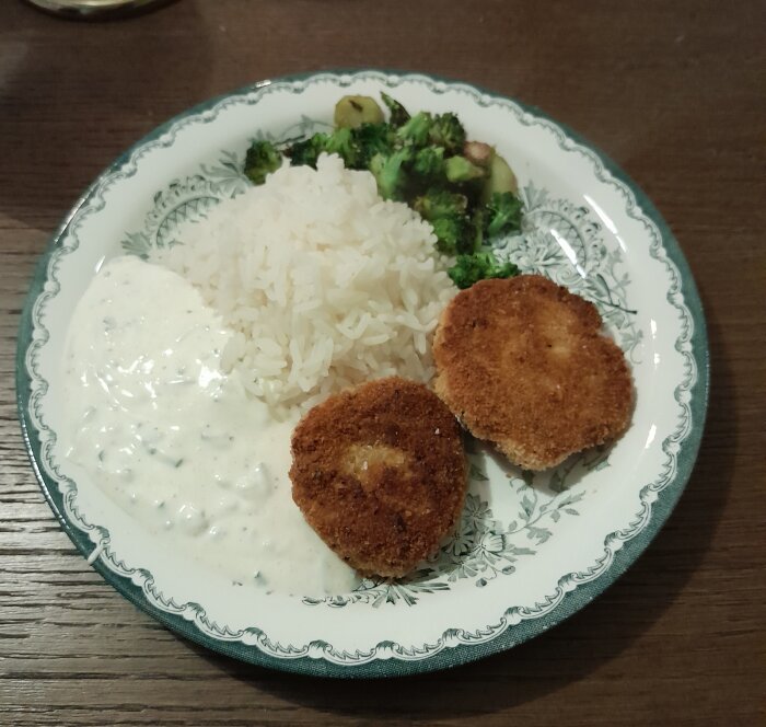 Middagstallrik med ris, broccoligrönsaker, panerade kycklingfiléer och vitlöksås på dekorativ tallrik.