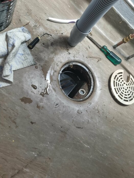 Diskbänk med öppen avloppsrörinstallation, verktyg och skräp runtomkring.