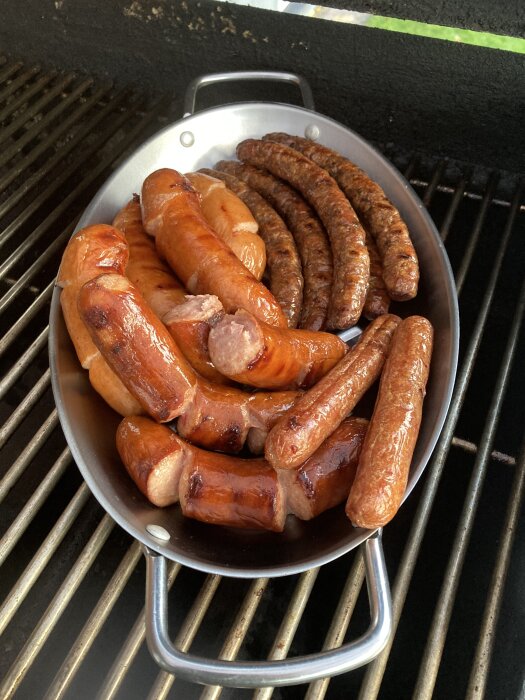 Grillade korvar i grå panna på grillgaller. Olika storlekar och bränningen, bbq-tema, matlagning utomhus.