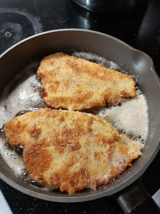 Två panerade schnitzlar steks i en stekpanna på spisen.