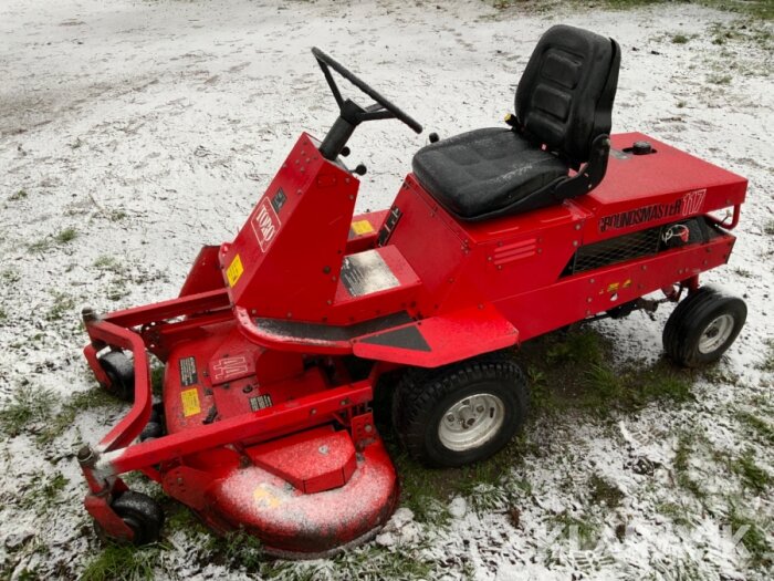 Röd åkgräsklippare på gräsmatta med lite snö.
