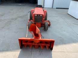 Röd kompakt traktor med frontmonterad snöslunga på en asfalterad yta.