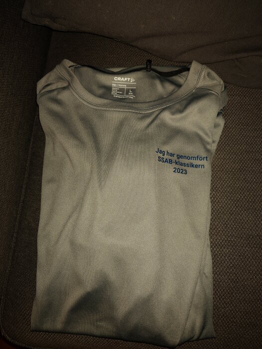 Grå Craft t-shirt, text "Jag har genomfört SSAB-klassikern 2023", storlek L, ligger på brun yta.
