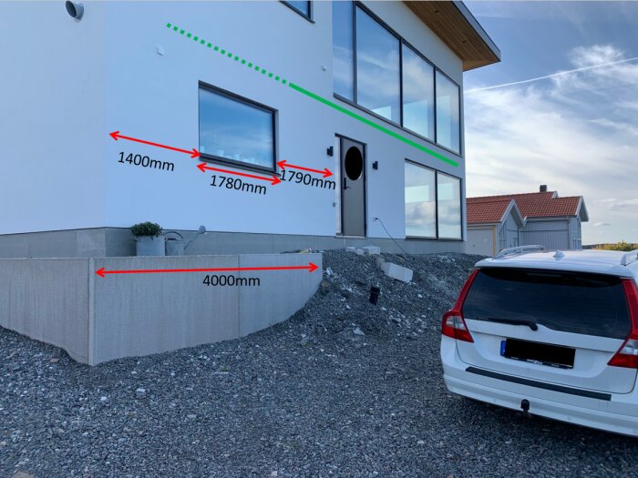 Modernt hus med mätningar för fönster och väggmarkerad, parkerad bil framför, byggzone, grusuppfart.