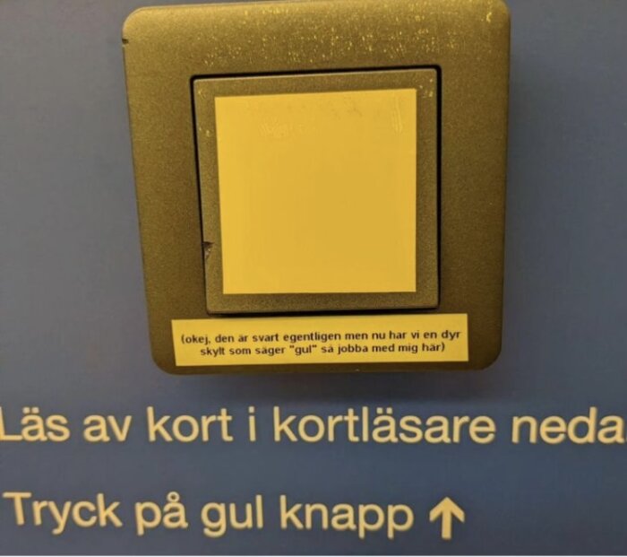 Gul skylt på elektronisk enhet med text och instruktioner, humoristisk kommentar, blå bakgrund.