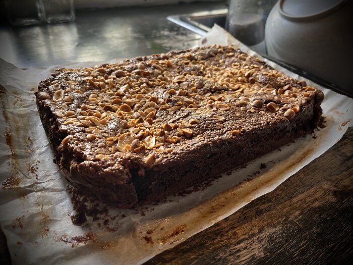 Fuktig chokladkaka med hackade nötter på ett bakplåtspapper, köksbänk i bakgrunden, hemtillverkad dessert.