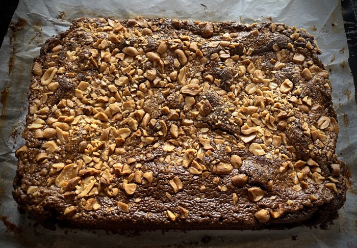 Fyrkantig bakelse med nötter, ser ut som brownie eller kladdkaka på bakplåtspapper.