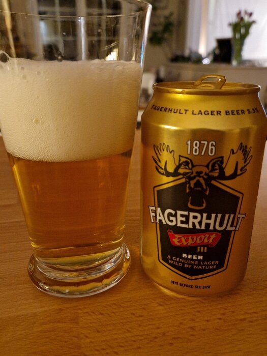 Ett glas öl med skum och en Fagerhult lagerburk på bordet. Inomhusmiljö.