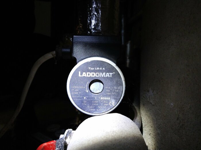Cirkulationspump märkt "LADDOMAT", elektrisk ledning, delvis mörk bakgrund, teknisk utrustning.