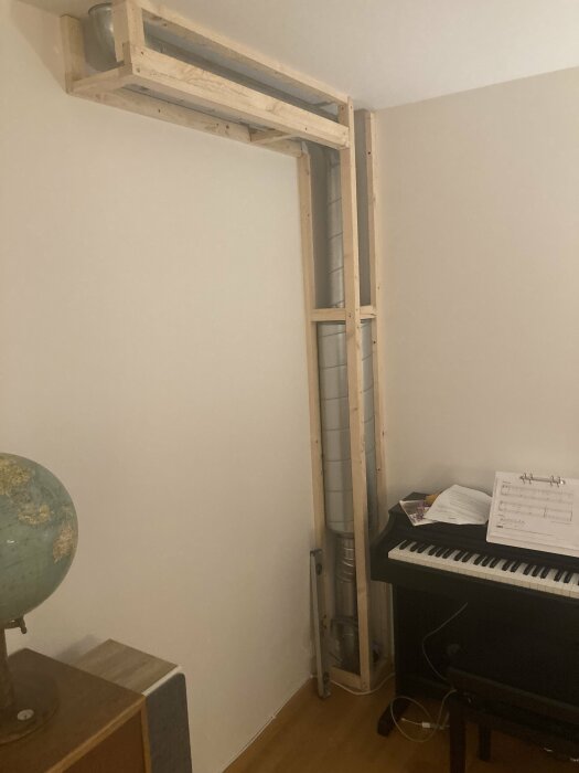 Ett hörn av ett rum med digitalpiano, glob och träkonstruktion i taket.