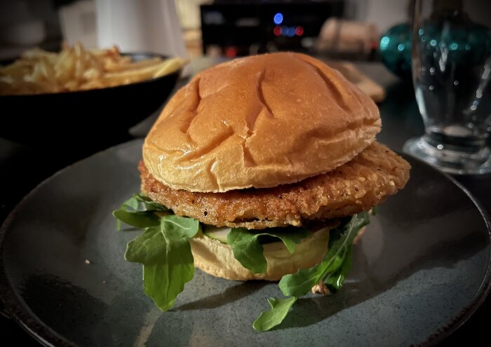 En saftig hamburgare med grönsallad och stekt biff på en mörk tallrik, bakgrundsoskärpa visar pommes frites.