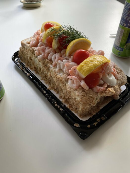 Ett smörgåstårta med räkor, citron, dill och cocktailtomater på ett vitt bord.