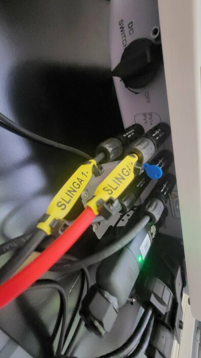 Kablar märkta "SLINGA 1", strömbrytare, rörig teknisk utrustning, ljusindikator lyser grönt.