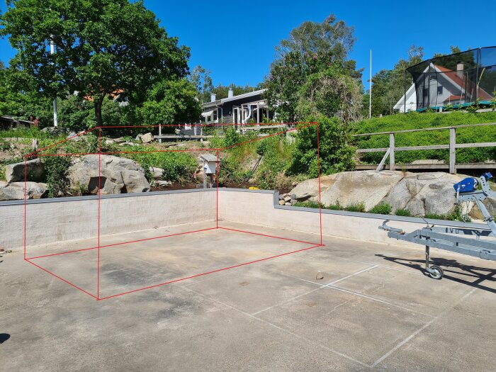 Utomhus padeltennisbana under konstruktion, betonggrund, gröna träd, släpvagn i förgrunden.