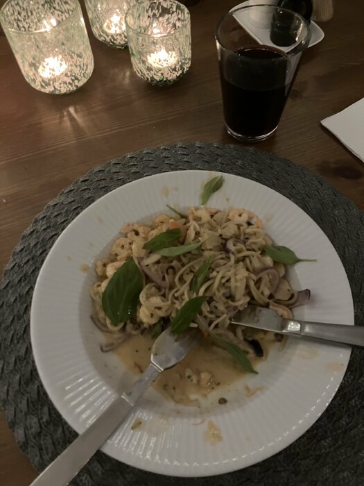 Middag med pasta, sås och basilika, ljus i bakgrunden, ett glas mörk dryck.