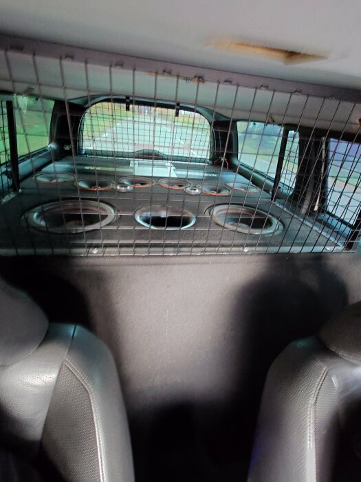Baksätet på en bil med hundbur och skålar, skyddsnät mellan baksäte och lastutrymme.