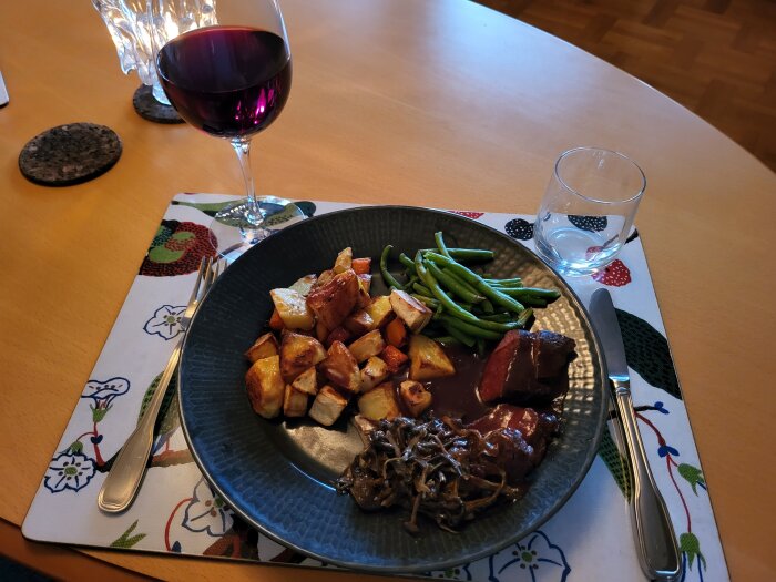 Ett måltidsarrangemang med rött vin, gröna bönor, stekt potatis, kött och svamp på ett dukat bord.