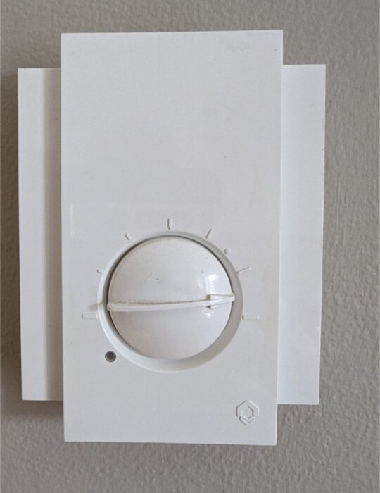 Väggmonterad termostat med vridknapp och temperaturindikatorer på en texturerad yta.