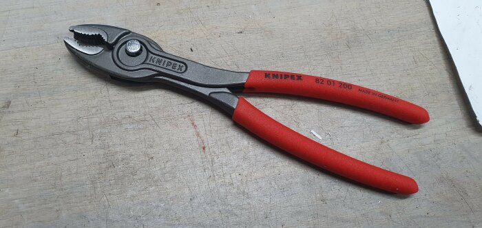 Knipex vattång på arbetsbänk, röda handtag, märkt "Made in Germany", slitage, använd för greppa, vrida, klämma.
