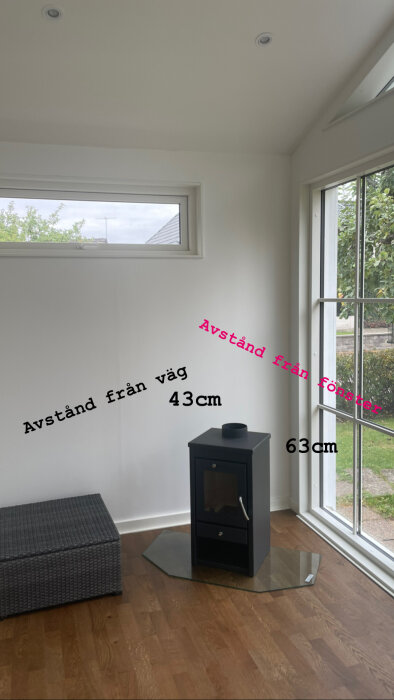 Ett modernt rum med korgstol, ugn/eldstad, fönster och uppmätta avstånd markerade på bilden.