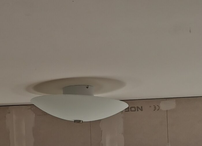 Vitt tak med modern lampa, ojämna väggar som verkar under renovering.