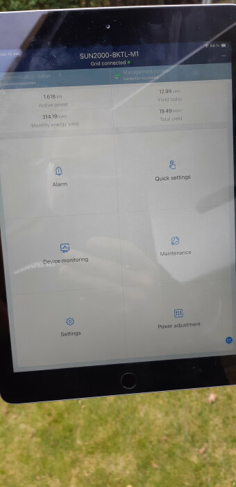 En skärm som visar data för en grid-connected enhet, energiproduktion, inställningar, med gräs i bakgrunden.