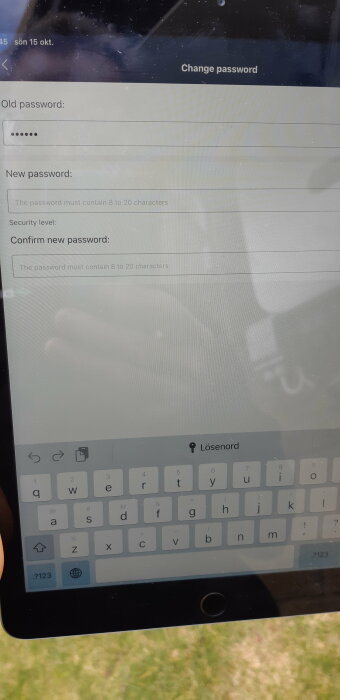 Skärmbild visar lösenordsändring, digital tangentbord, reflektion av person, utomhus, dagtid, text på svenska.