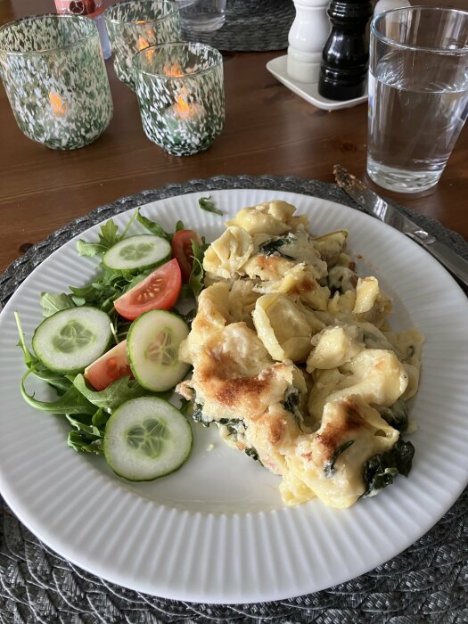 Gratinerad pasta med spenat, sallad med gurka och tomat, ljusstakar, salt- och pepparkvarnar, vattenglas på bordet.