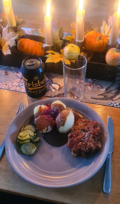 Mysig middagsbild med stearinljus, pumpor, ölburk, maträtt med köttbullar, potatis och inlagd gurka.