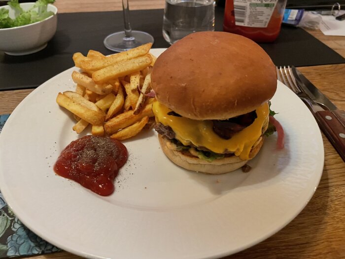 Cheeseburgare med pommes och ketchup på en vit tallrik, bordsservering.