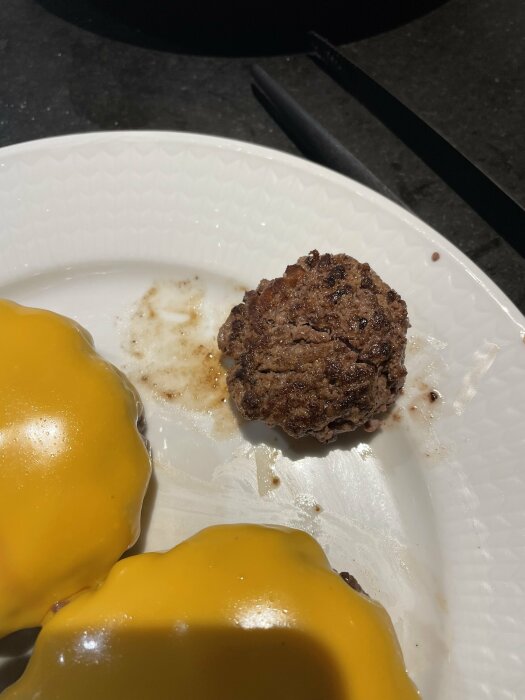 Stekt köttbulle och två portionsostar på en vit tallrik med en kniv.