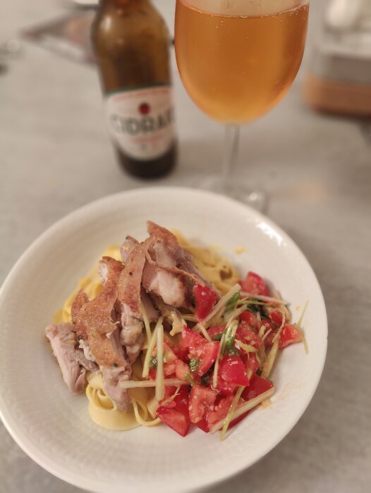 Middag med pasta, kyckling, tomater och ärtskott, serverad med cidervin i bakgrunden.