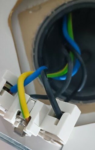 Elektrisk installation, färgkodade kablar, säkerhetsbrytare, otydlig bakgrund, arbete pågår, vita och svarta plastdetaljer.