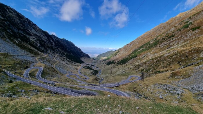 Vindlande väg i bergsdal med skarpa kurvor och vacker utsikt under blå himmel.