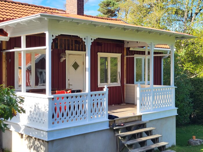 Rött trähus med vit veranda, grönskande trädgård, sommardag, soligt, mysigt, traditionell svensk stil.