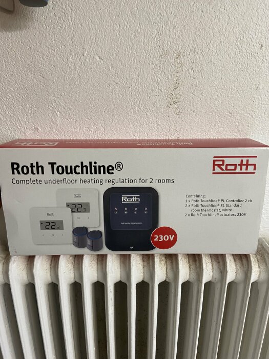 Förpackning för Roth Touchline golvvärmereglering framför en vit radiator mot en vägg.