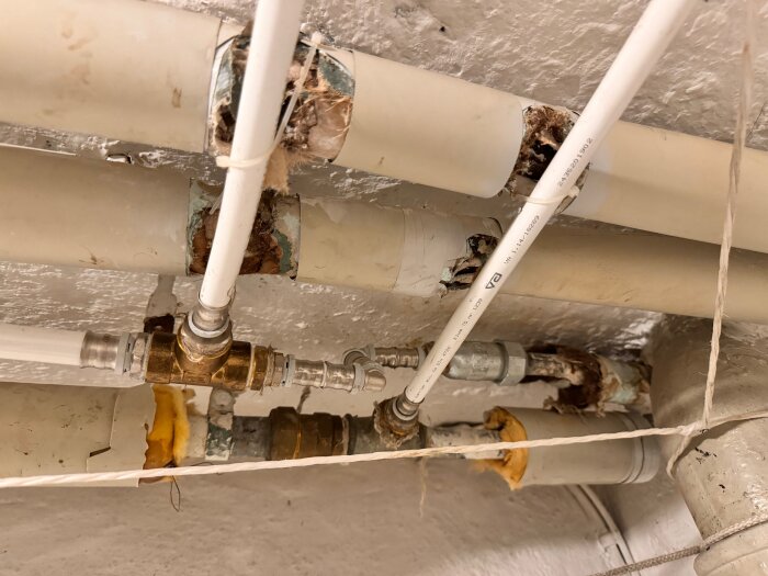 Vattenledningar och ventiler under taket, korroderade och med tecken på läckage eller vattenskada.