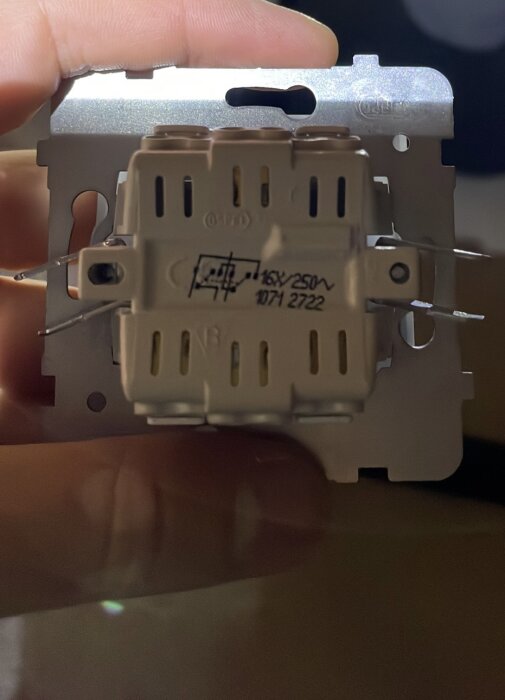 Elektrisk komponent, troligen en brytare eller kontakt, med tekniska specifikationer synliga, hand håller fast den.