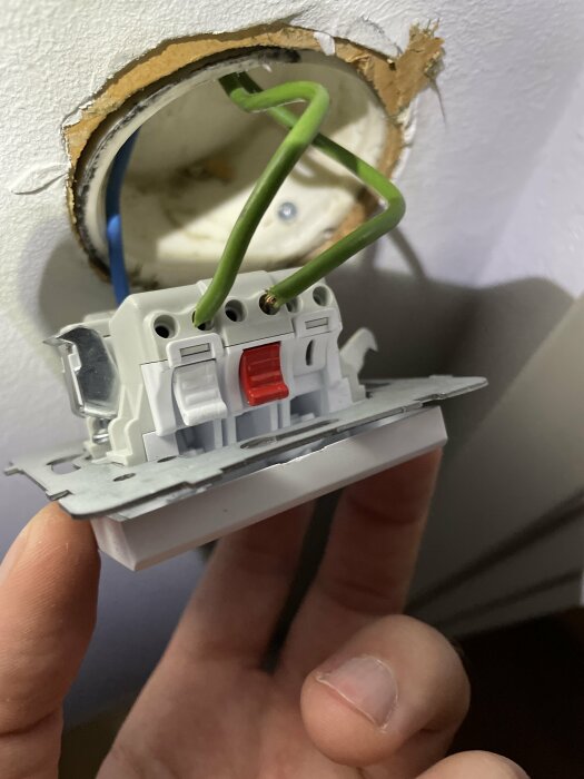 Eluttag hålls, osäker elledning, ojämn väggöppning, installationsarbete, säkerhetsrisk, närbild, konstruktionsdetaljer.