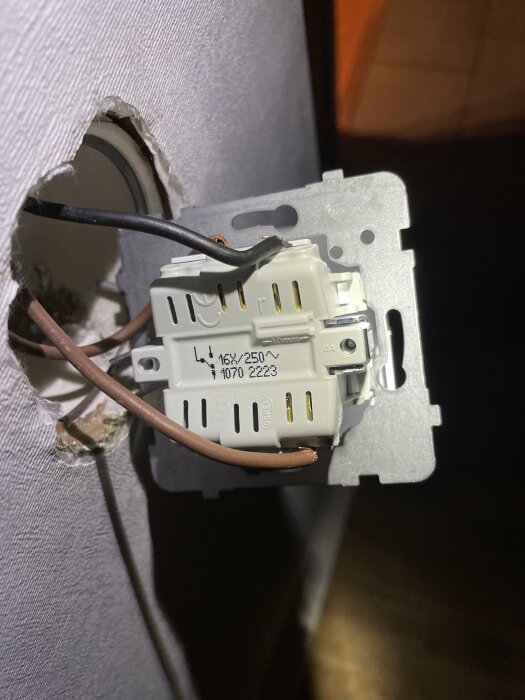 Öppen elektrisk vägguttag, kablar synliga, installation pågår eller skadad, säkerhetsrisk, ojämnt hål i väggen.