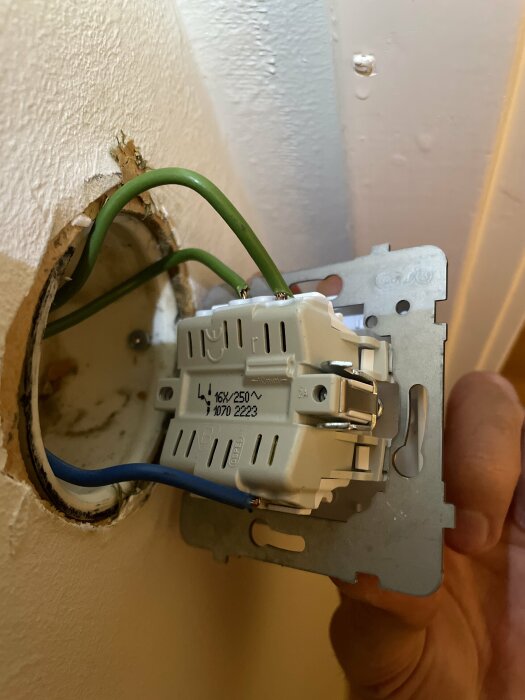 Eluttag halvt inbyggt i vägg, osäker anslutning, synliga ledningar, risk för elchock, installationsarbete pågår.