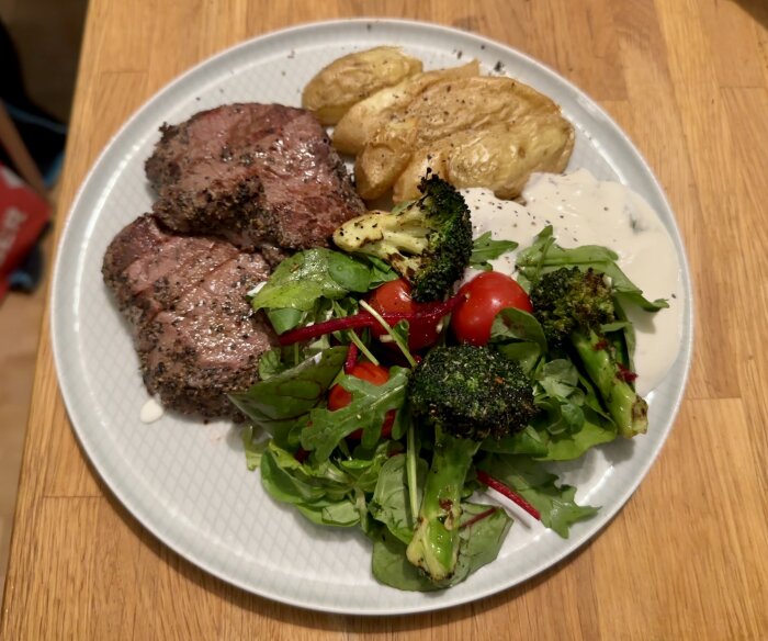 Middagstallrik med biff, sallad, rostad broccoli, potatis och gräddsås.