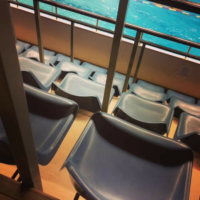 Tomma åskådarplatser framför en simbassäng i en idrottsanläggning.