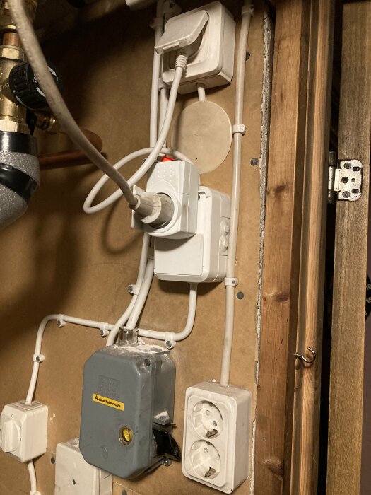 Elektriska installationer, säkerhetsbrytare, sladdar och kontakter på en vägg med synliga rörledningar.