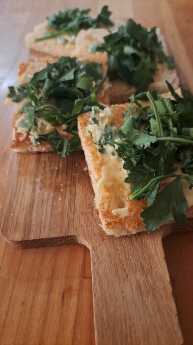 Smörstekta brödbitar med smält ost och färsk persilja på träskärbräda.