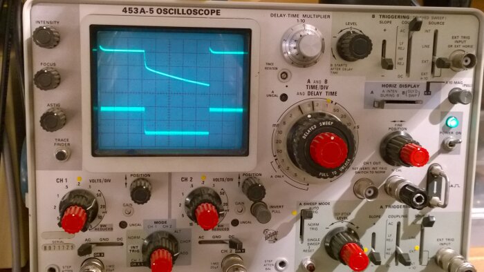 Analogt oscilloskop med vågform på skärmen. Knappar och justeringsrattar syns tydligt. Instrumetent för elektrisk signalanalys.