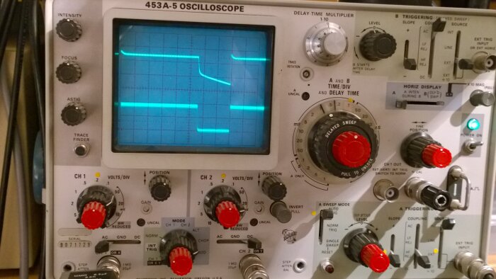 Analogt oscilloskop med vågform på skärmen, många reglage och knappar, elektronikmätutrustning.